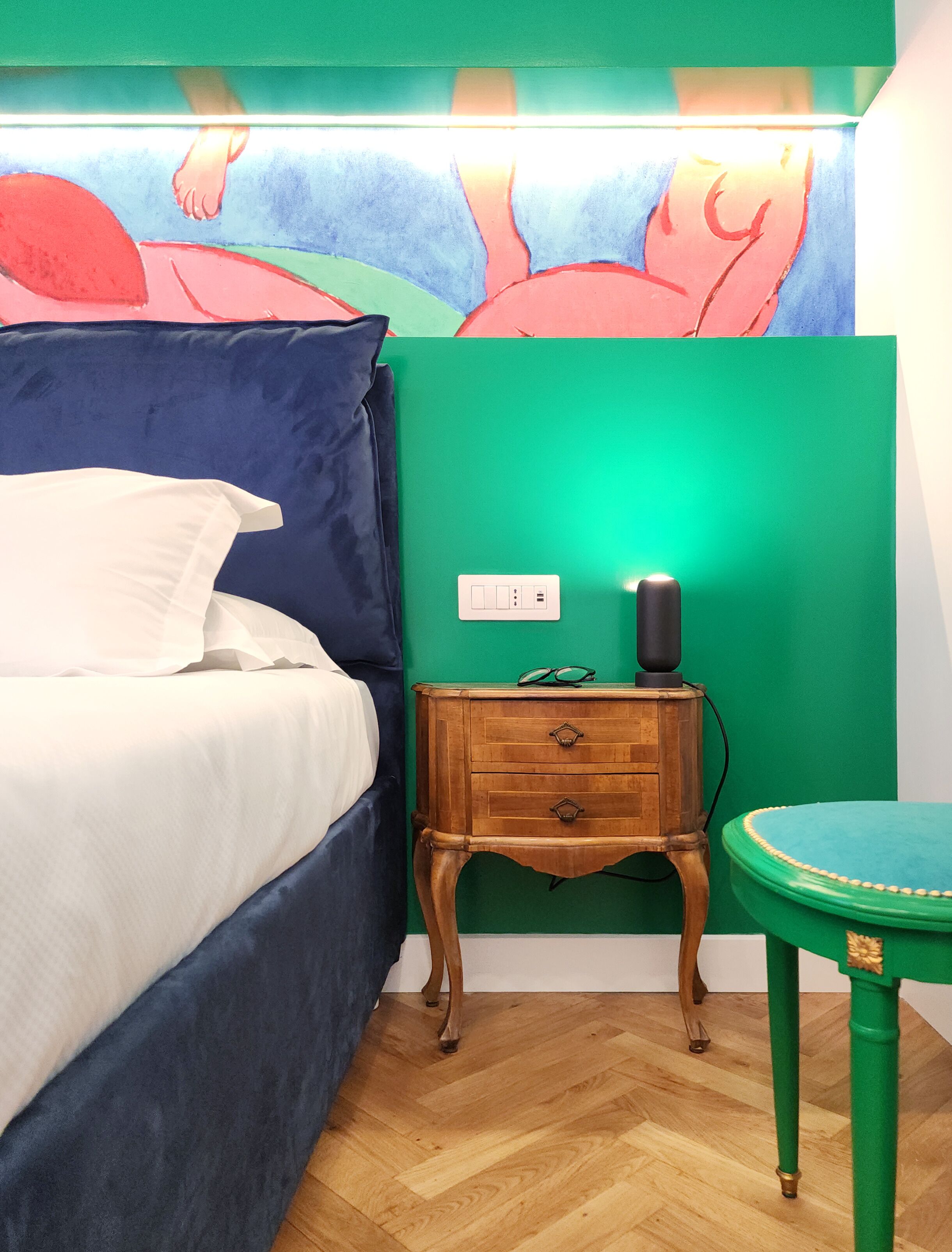 Een slaapkamer met een bed, nachtkastje en een groene muur met een schilderij.