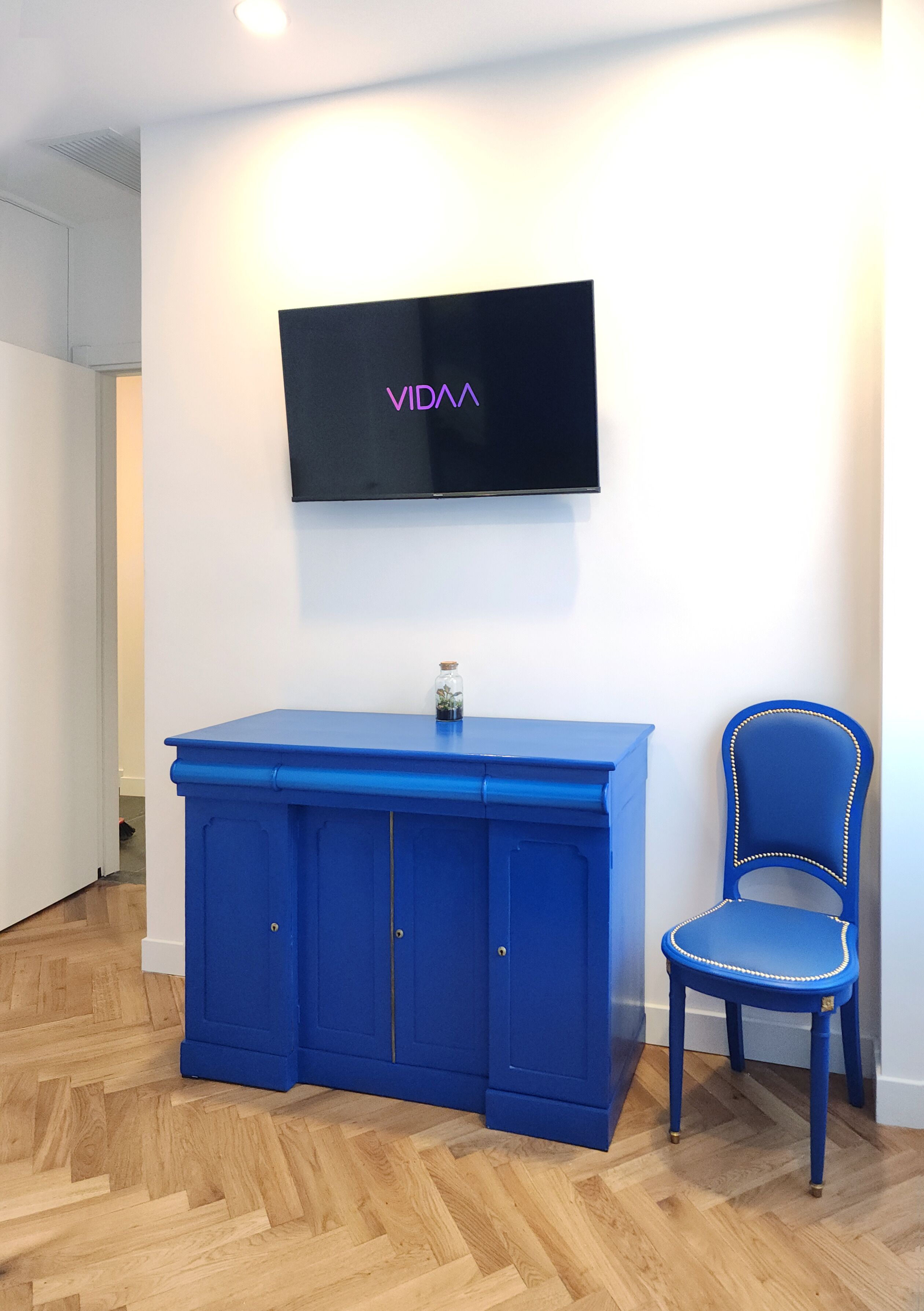 Une pièce avec un meuble bleu, une chaise bleue et un téléviseur à écran plat fixé au mur, qui affiche le mot « VIDA ».