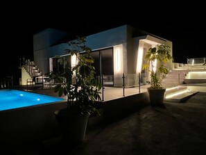 A modern building with a pool, potted plants, and a staircase leading to an upper level.