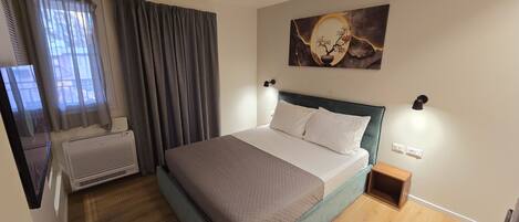 A neatly arranged bedroom with a bed, a wall-mounted artwork, and a small bedside table.
