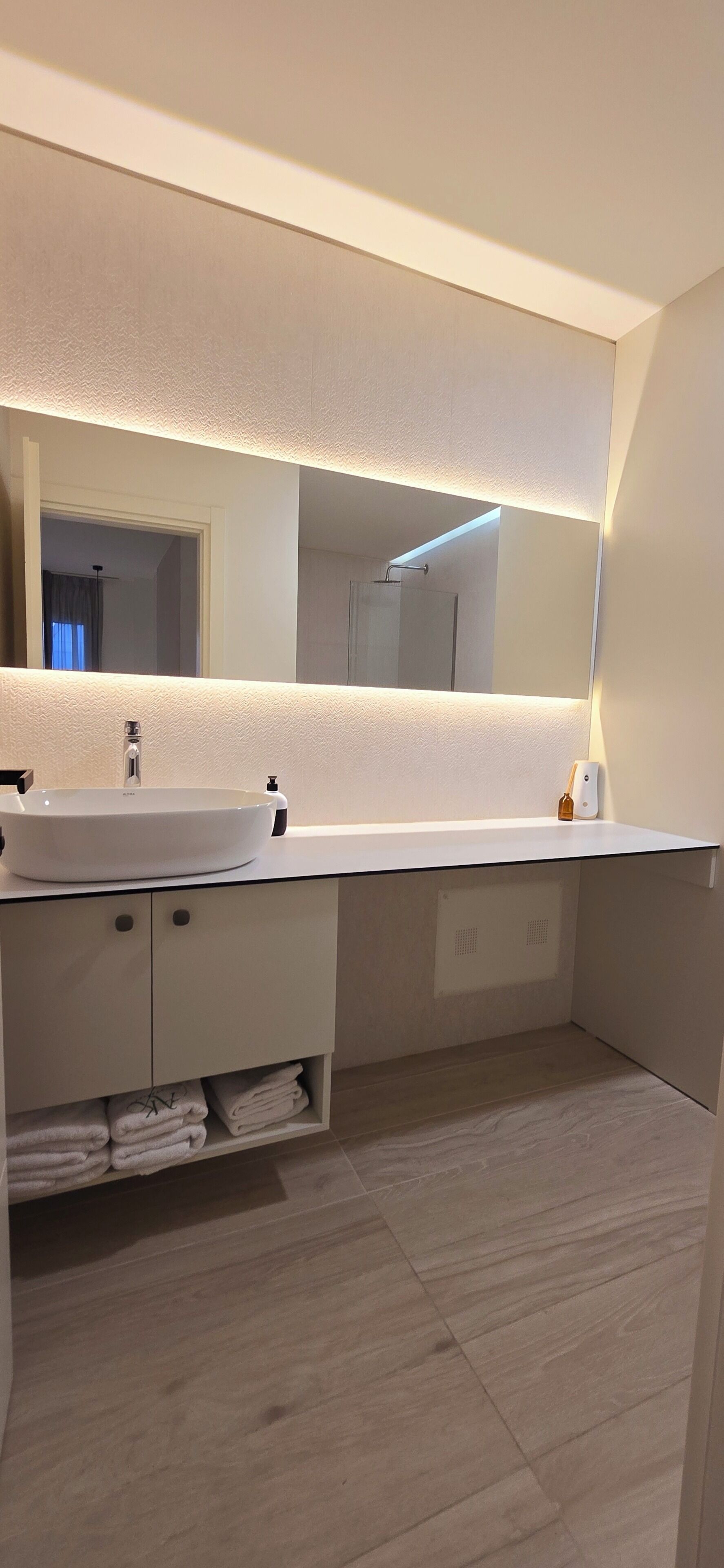 Un baño moderno con un espejo grande, un lavabo blanco y un perchero para toallas.