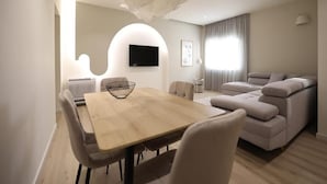 A modern living room with a wooden dining table, a sofa, and a TV mounted on the wall. - Arkle Apartment 4 (Tirana)