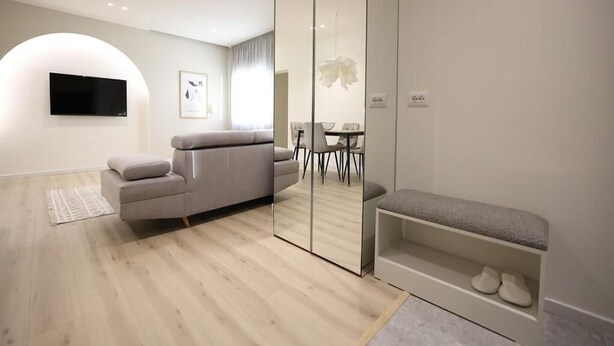 A modern living room with a sofa, a bench, a television, and a dining area. - Arkle Apartment 4 (Tirana)