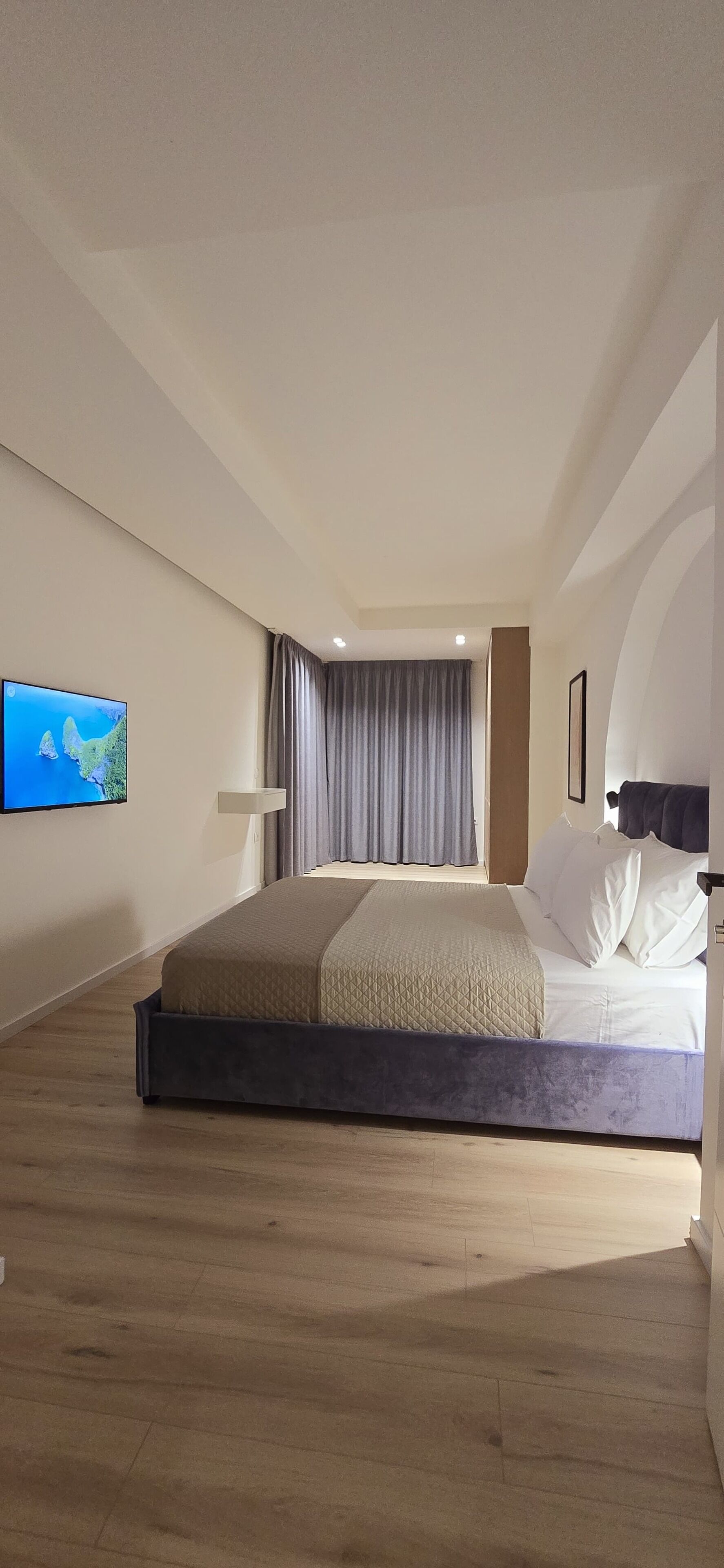 Ein modernes Hotelzimmer mit einem großen Bett, einem flachbildfernseher an der Wand und einem großen Fenster mit Vorhängen.