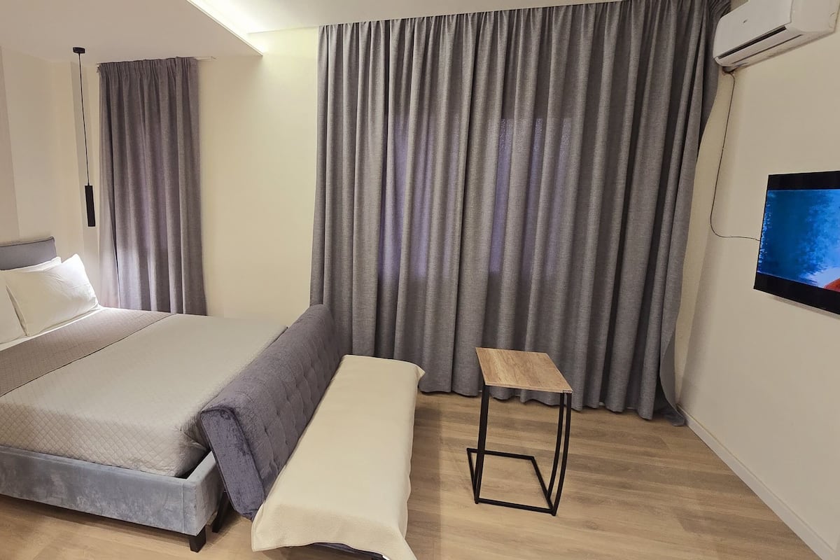 Una habitación de hotel moderna con cama, un banco, un televisor y cortinas.