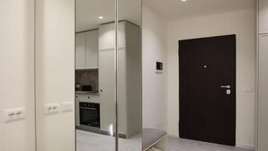 A modern room with a large mirror, a black door, and a visible kitchen area in the background. - Arkle Apartment 4 (Tirana)