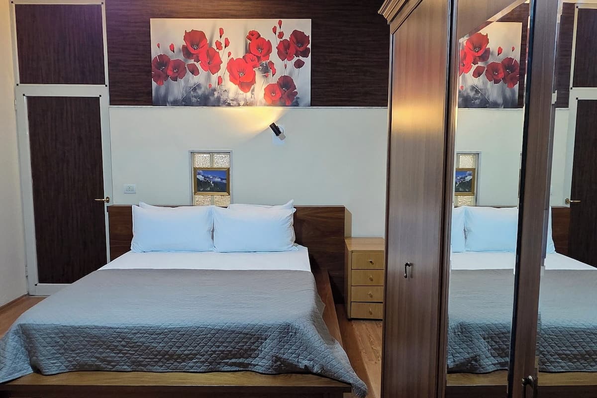 Un dormitorio con cama, suelo de madera, una lámpara de pared, un espejo y un cuadro.