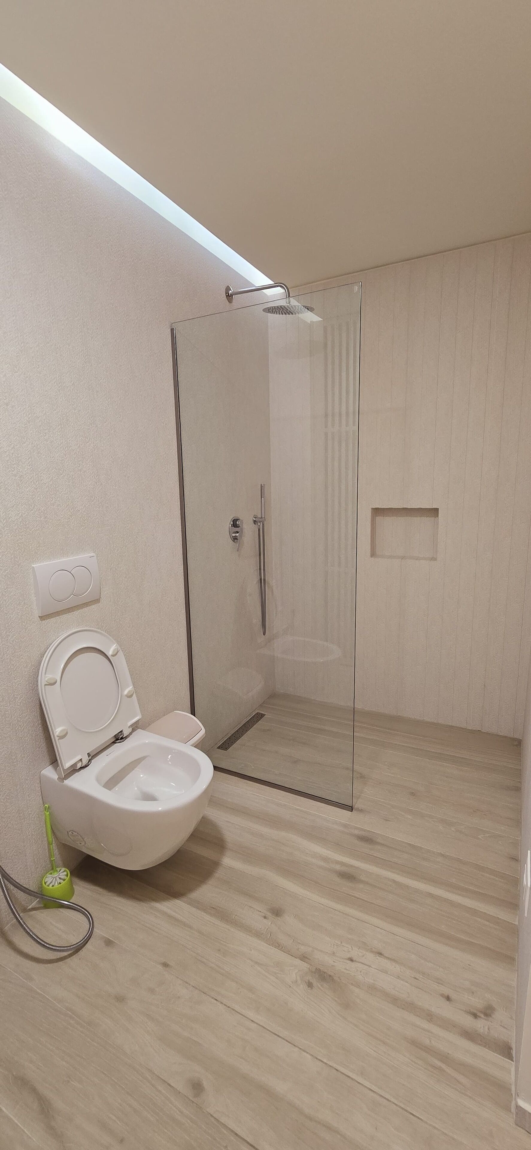 Un baño moderno con ducha acristalada, inodoro blanco y suelo de madera.