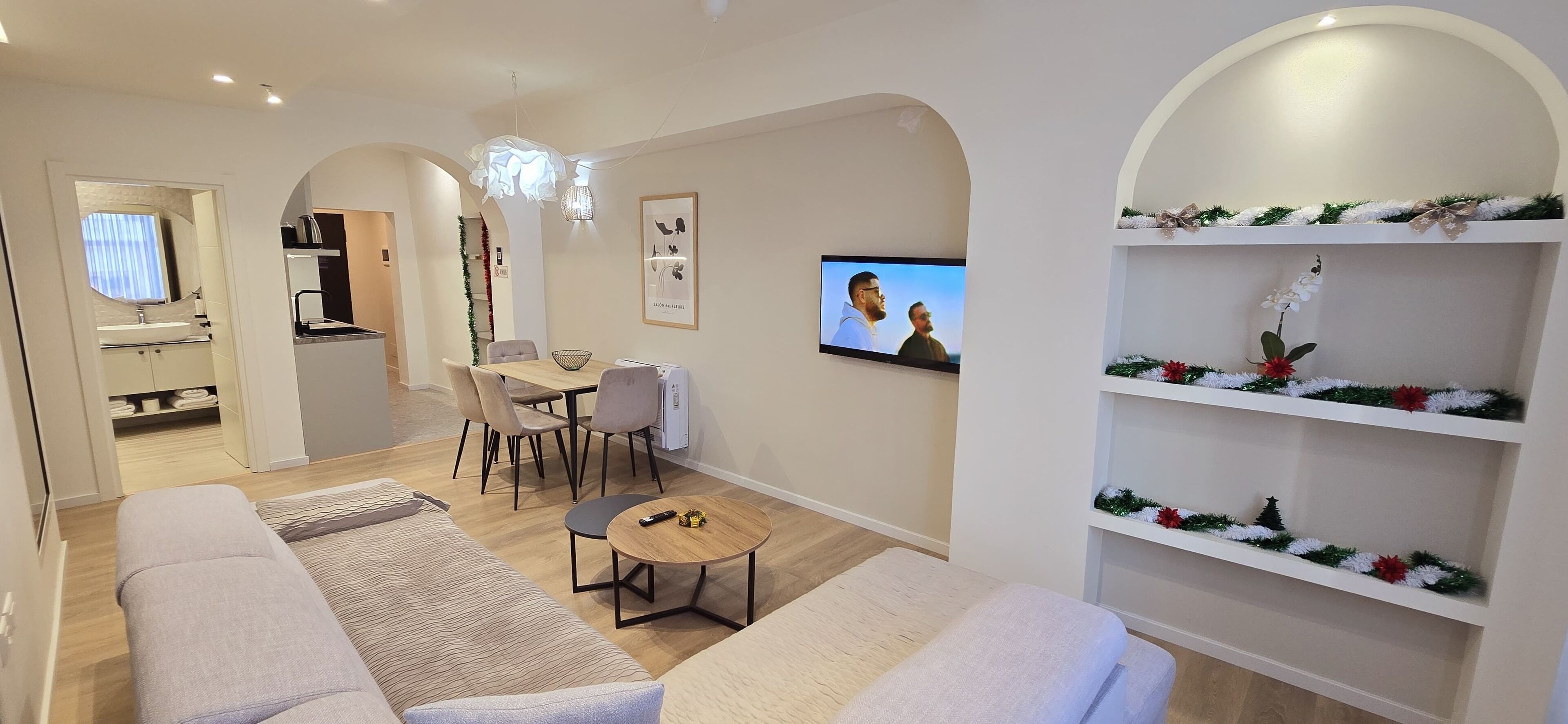 A modern living room with a sofa, a dining table with chairs, a TV, and a bookshelf with holiday decorations.