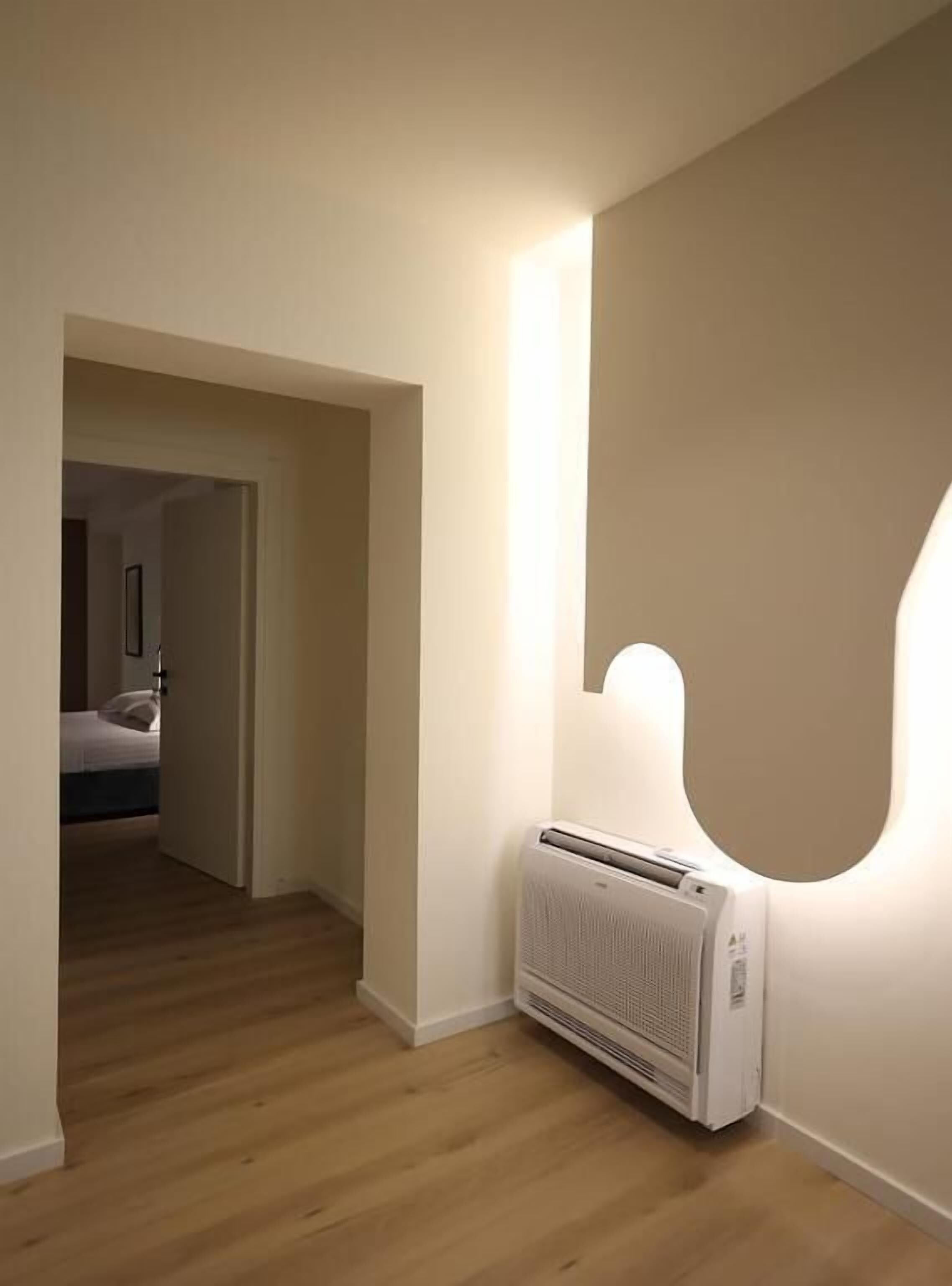 Un couloir avec un radiateur, un plancher en bois et une porte donnant sur une chambre.