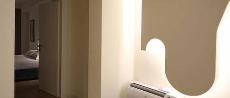 Un couloir avec un radiateur, un plancher en bois et une porte donnant sur une chambre.
