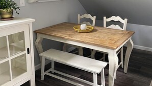 Un coin repas avec une table en bois, des chaises blanches, un banc et une plante en pot.