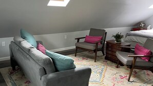 Une chambre de style loft avec un canapé gris, deux fauteuils, une commode et une lucarne.