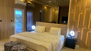 Une chambre à coucher avec un grand lit, deux lampes de chevet, un pouf à motifs zébrés et un panneau mural en bois.