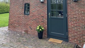 A brick building with a dark door, two windows, and a small potted plant. - Special design apartment in the countryside for your time out in the north (Wangerland)
