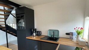A modern kitchen with a wooden countertop, black cabinets, a built-in oven, and a small sink. - Special design apartment in the countryside for your time out in the north (Wangerland)