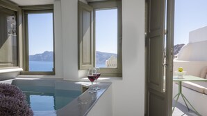 Una habitación con bañera, una copa de vino tinto y vista al mar.