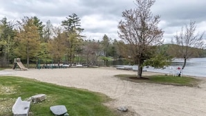 Ein Strandabschnitt mit Sand, einem Spielplatz, einem Baum und einem See.