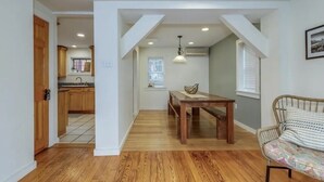Ein modernes Interieur mit einem Holzesstisch, einer Couch und einer durch einen offenen Durchgang sichtbaren Küche.