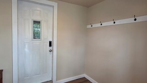 A room with a white door, a small window, a white wall, and a white shelf with hooks.
