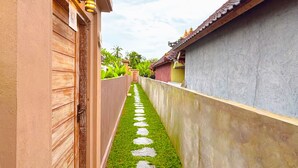 Un étroit sentier bordé d’une pelouse verdoyante et de dalles, avec des bâtiments aux façades variées de chaque côté, et un ciel dégagé au-dessus.