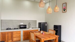 Une cuisine moderne équipée d’une cuisinière à gaz intégrée, d’un four à micro-ondes, d’un évier et d’un réfrigérateur. On y trouve des armoires en bois, une table à manger en bois avec des chaises, et trois lampes suspendues.