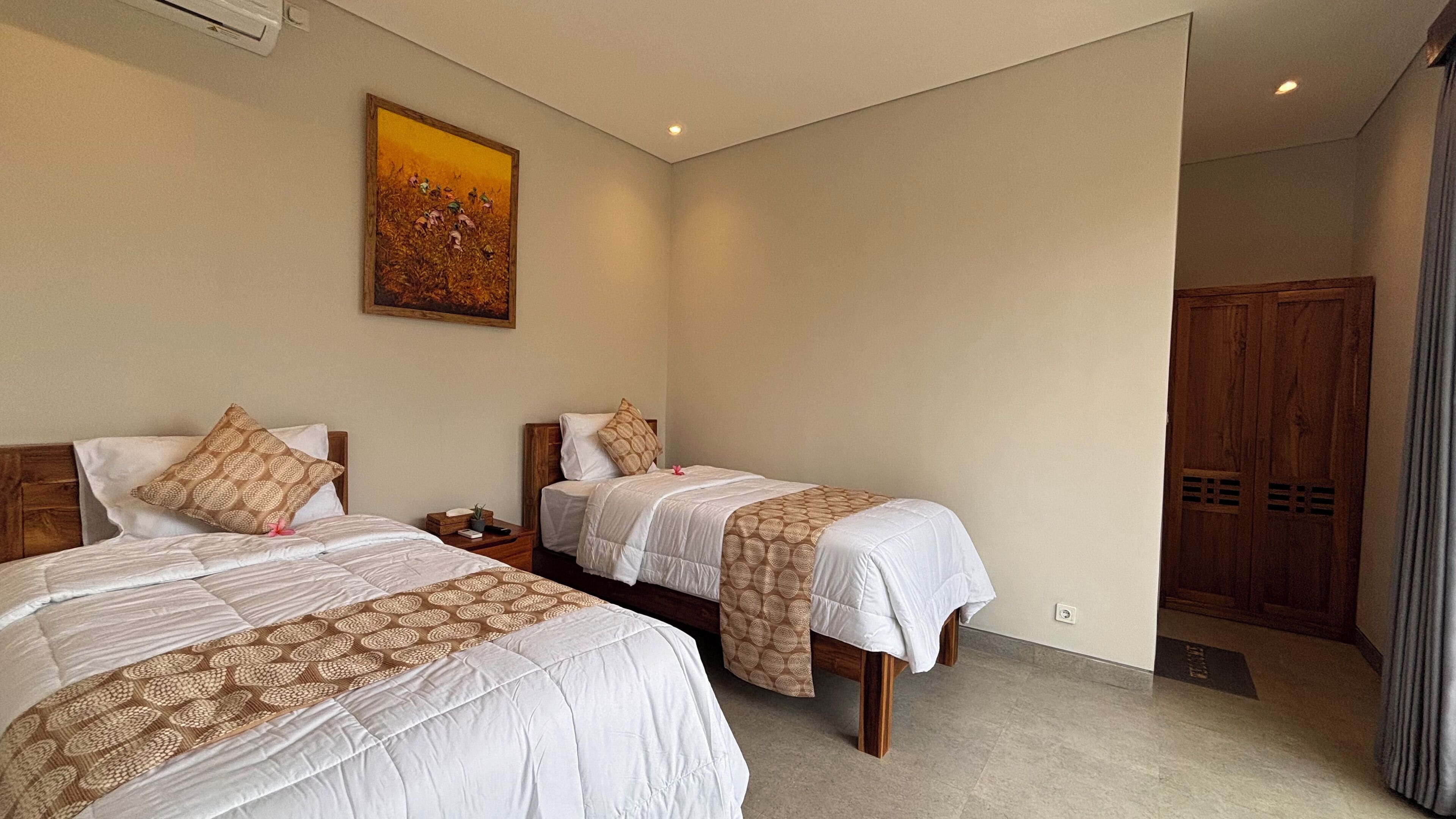 A hotel room with two beds, a painting on the wall, and a wooden wardrobe.