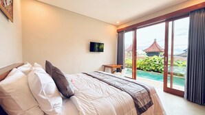 Une chambre avec un lit, une télévision, une petite table et une vue sur une piscine et des bâtiments traditionnels.