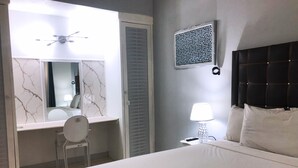A hotel room with a bed, a desk with a chair, a mirror, a bedside lamp, and a decorative wall panel. - Beach and Bliss E32 - Ocho Rios Retreats (Ocho Rios)