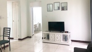 A living room with a TV on a white cabinet, a black chair, and a white door. - Beach and Bliss E32 - Ocho Rios Retreats (Ocho Rios)