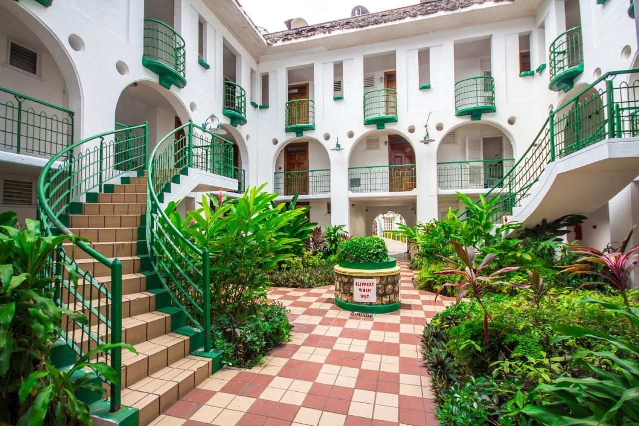 A courtyard with a checkered floor, green railings, and a central planter with a sign.