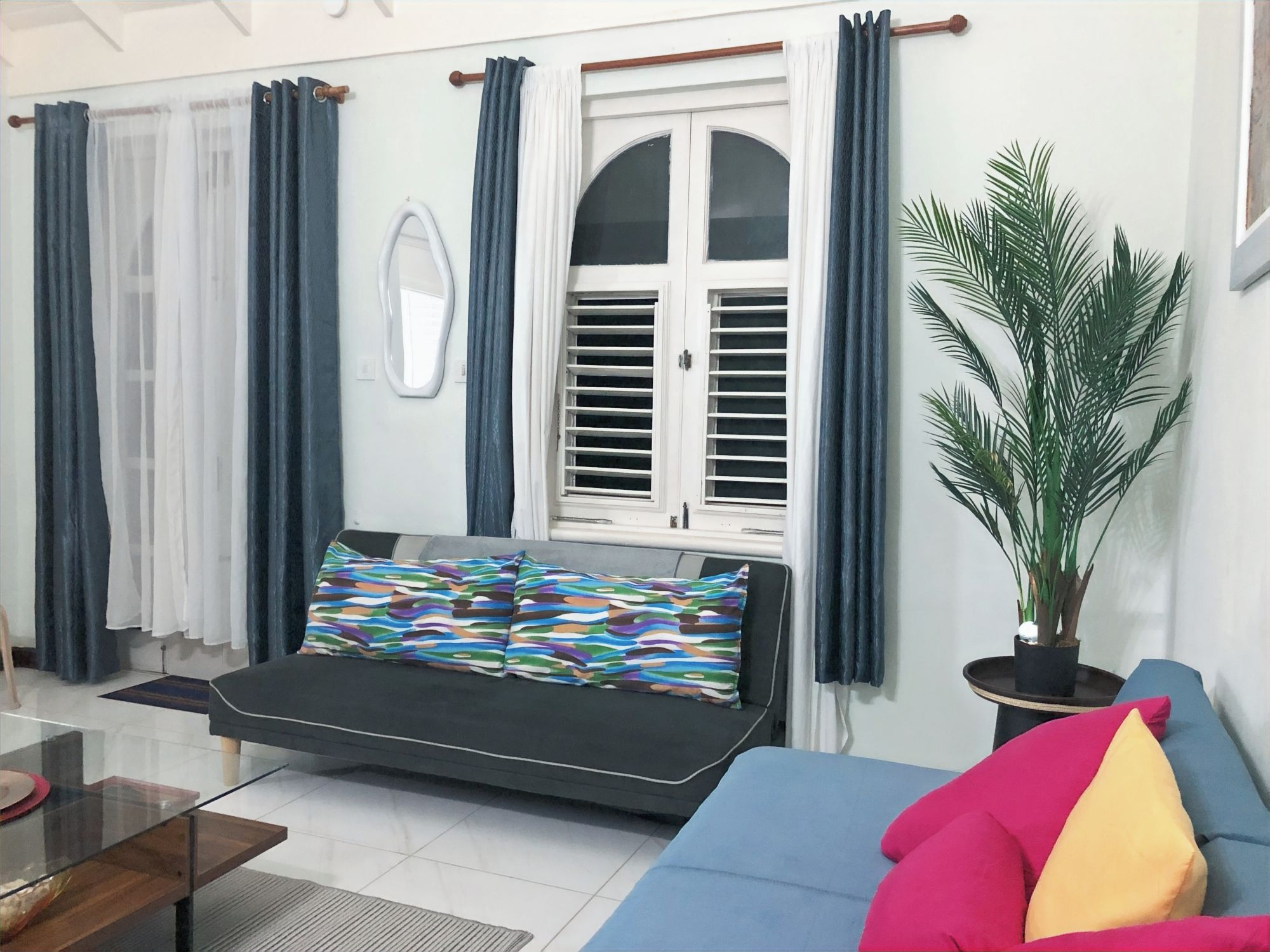 A living room with a sofa, a coffee table, a potted plant, and a window with curtains.