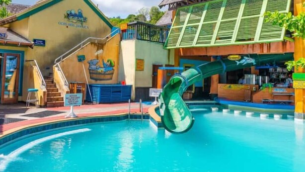 A pool with a water slide, a staircase, and a building with a sign that reads "Coco's 3306 Jamaica". - Beach and Bliss E32 - Ocho Rios Retreats (Ocho Rios)