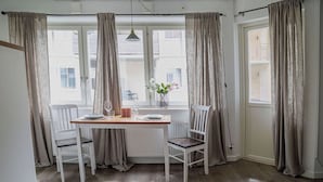 A dining area with a table set for two, white chairs, a vase with flowers, and a view through the window. - GotlandStay Volontären (Visby)