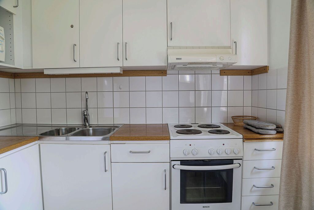 Ett kök med vita skåp, en spishäll från Bosch och en diskho.