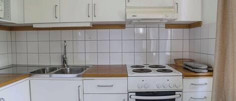 Ett kök med vita skåp, en spishäll från Bosch och en diskho.