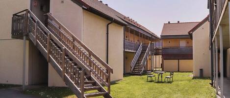 A building with a staircase leading to a covered area, a grassy courtyard, and a small seating area.