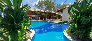 Piscina rodeada por vegetação exuberante e um edifício com várias varandas.