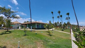 Una casa con techo verde, rodeada de un césped cuidado y varias palmeras.