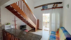 Un amplio salón con una escalera de madera, un televisor, un microondas y un sofá colorido.