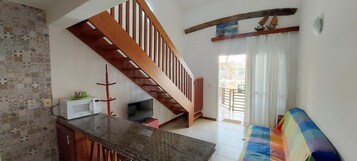 Uma sala ampla com escada de madeira, televisão, micro-ondas e um sofá colorido.
