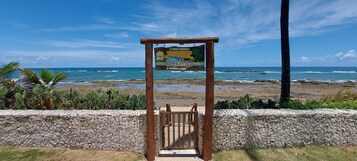 Entrada para a praia com uma placa indicando 'CONDIMINIO SAN SEBASTIAN' e vista para o oceano.