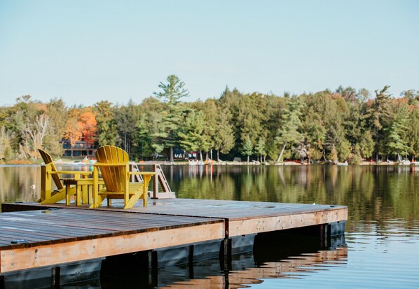 A wooden dock with yellow Adirondack chairs and a wooden table.