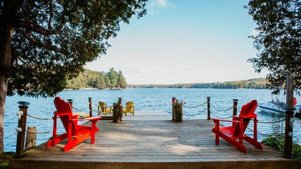 Una terraza de madera con sillas Adirondack rojas y amarillas que dan al lago.