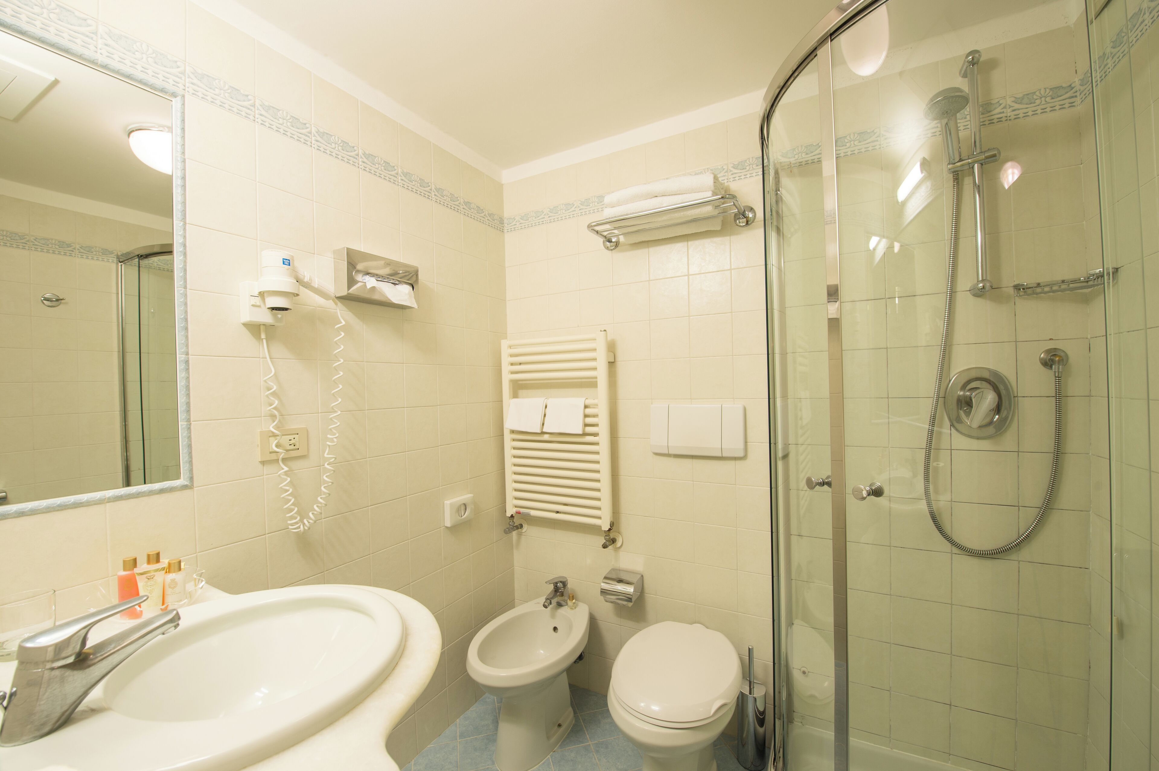 Et badeværelse med vask, bidet, toilet og en bruseafdeling med glasvægge.
