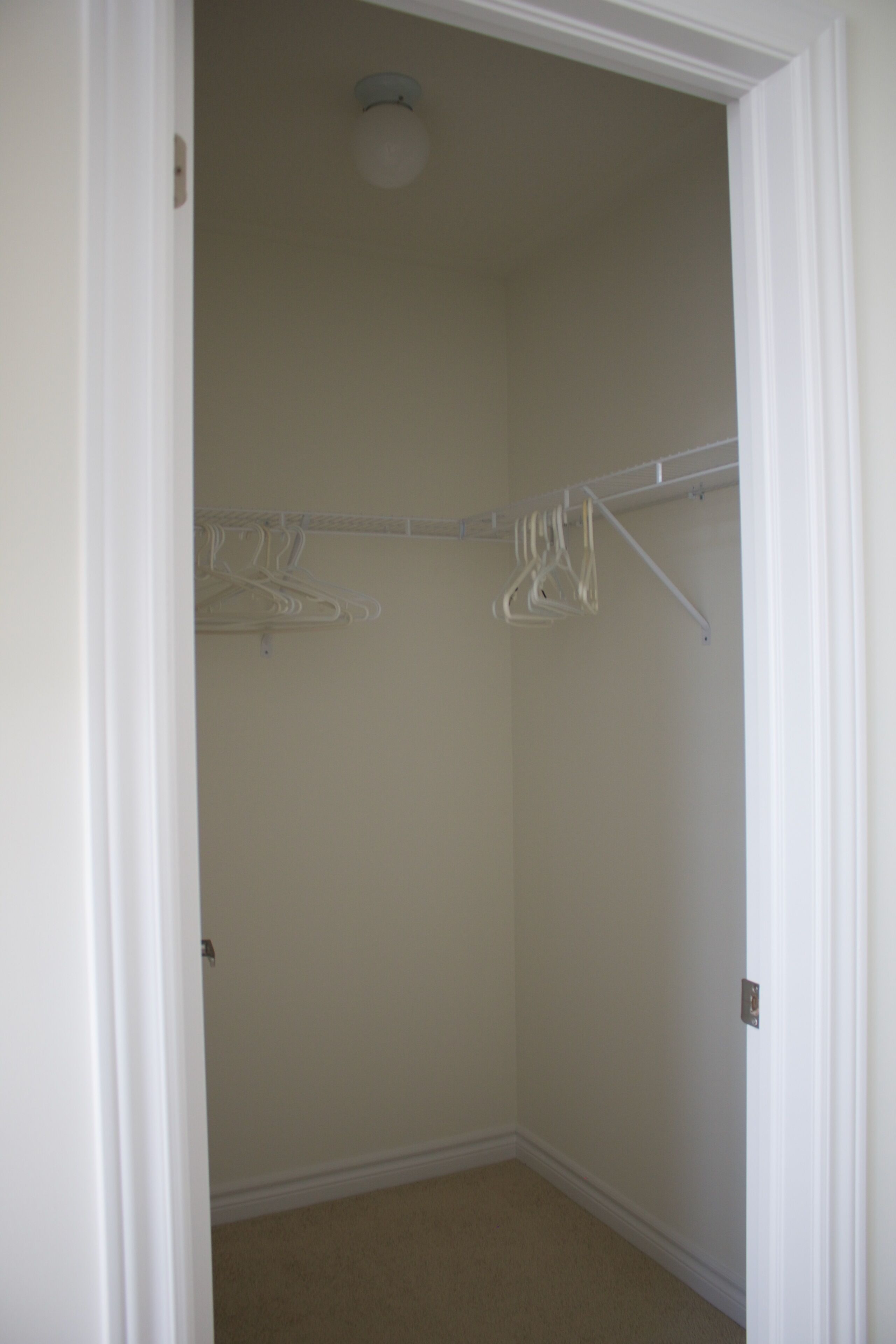 Un vestidor con puerta blanca, paredes color beige y una lámpara en el techo.