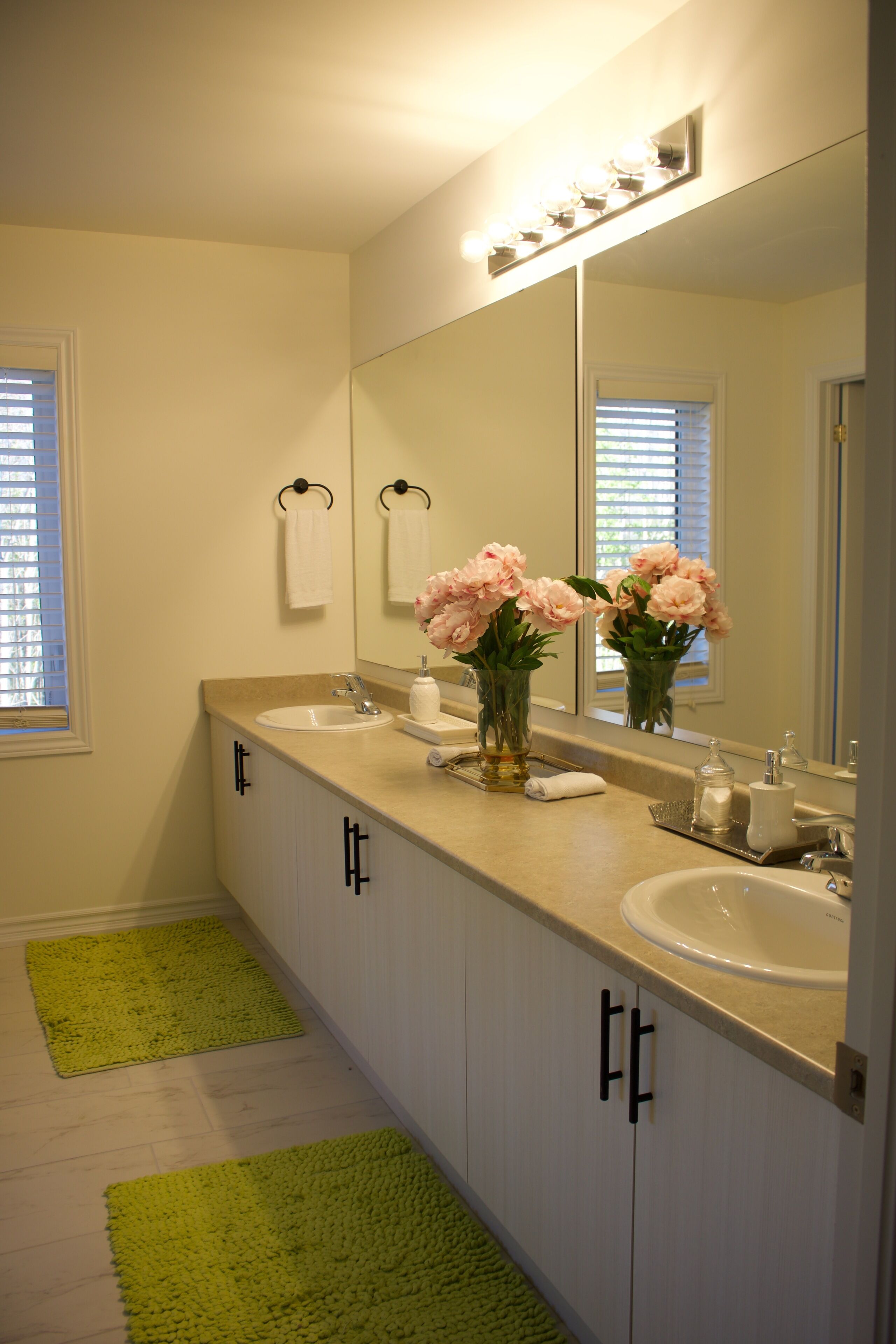 A bathroom with two sinks, a large mirror, and a green rug.