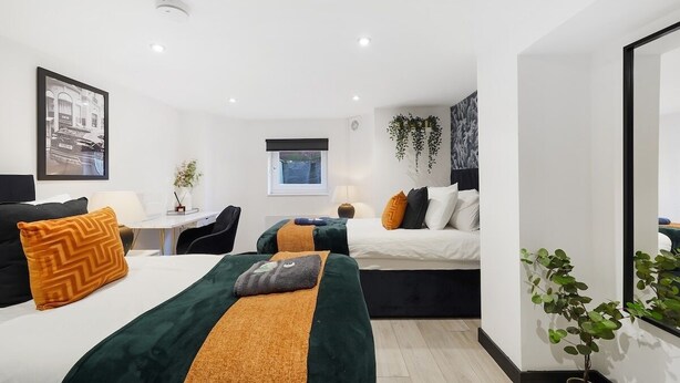 A modern hotel room with two beds, a desk, and a window.