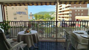 Un balcón con una mesa preparada para dos personas, con vistas a un hotel y un paisaje montañoso.