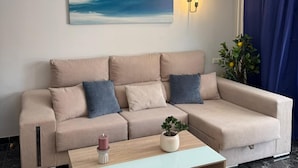 Una sala de estar moderna con un sofá seccional color beige, una mesa de centro de madera, una lámpara empotrada en la pared y un cuadro abstracto de gran tamaño.